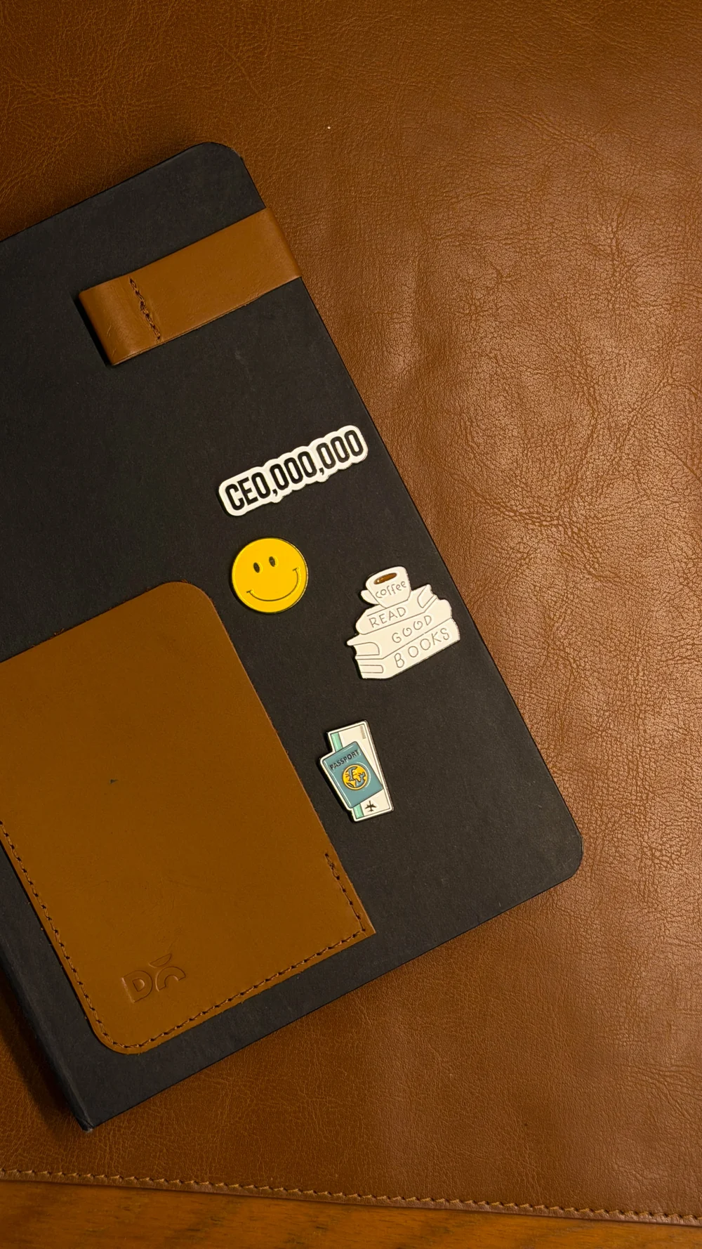 A black journal with smiley, books and passport enamel stickers